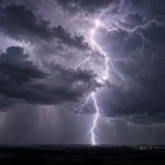 A bright, branching lightning bolt beneath dark thunderclouds over a distant town.